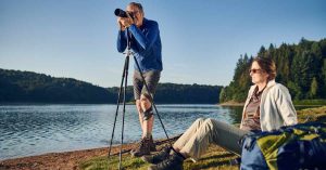 Man at the side of a lake taking a photo, wearing a knee brace